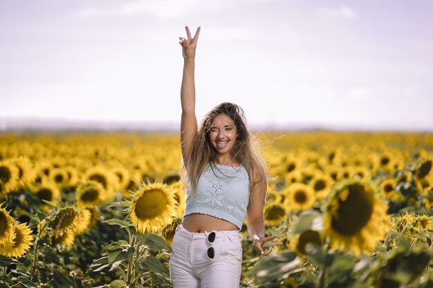 Foto horizontal de uma jovem mulher branca posando em um campo de girassóis em um dia ensolarado