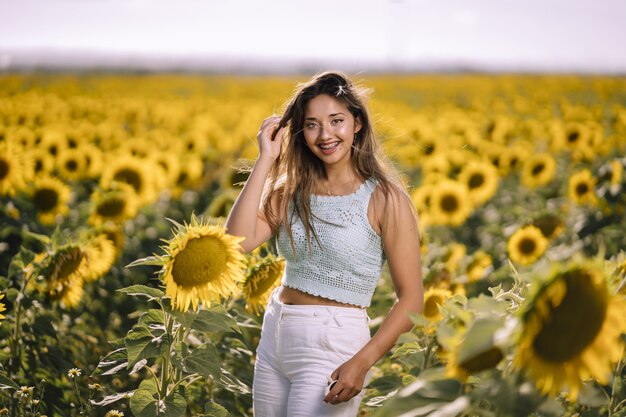 Foto horizontal de uma jovem mulher branca posando em um campo de girassóis em um dia ensolarado