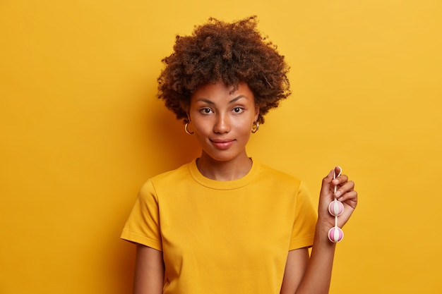 Foto grátis foto horizontal de uma mulher afro-americana usando bolas de kegel na corda para impulsionar a vida sexual, realiza exercícios regulares para fortalecer os músculos pélvicos da vagina, aumenta a sensação sexual antes do sexo com penetração