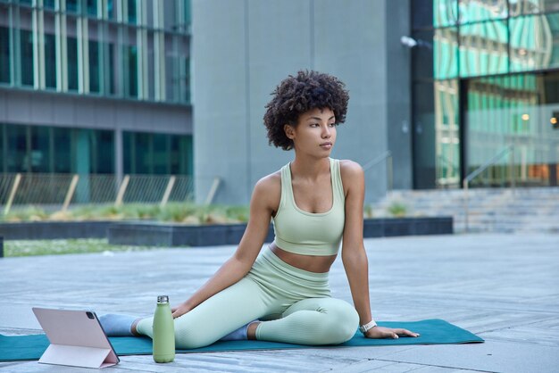 Foto horizontal de uma mulher pensativa e esportiva em poses de agasalho em relógios karemat sessão de treinamento via tablet