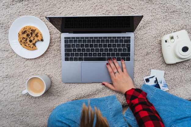 Foto horizontal de uma mulher sentada em um cobertor com seu laptop e café