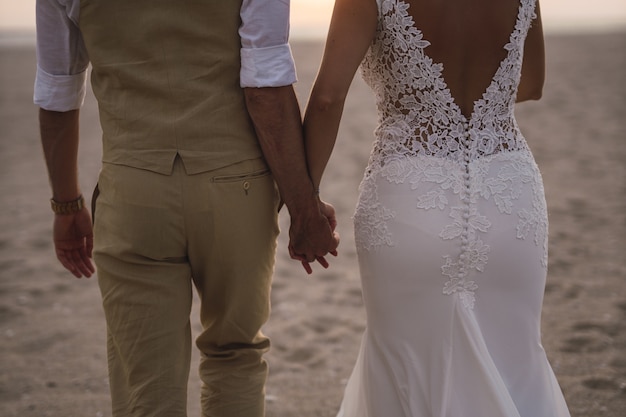 Foto horizontal de uma noiva e uma vassoura segurando as mãos uma da outra na praia