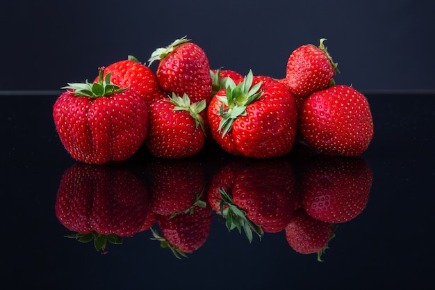 Foto horizontal de uma pilha de morangos vermelhos croatas em uma superfície preta refletora