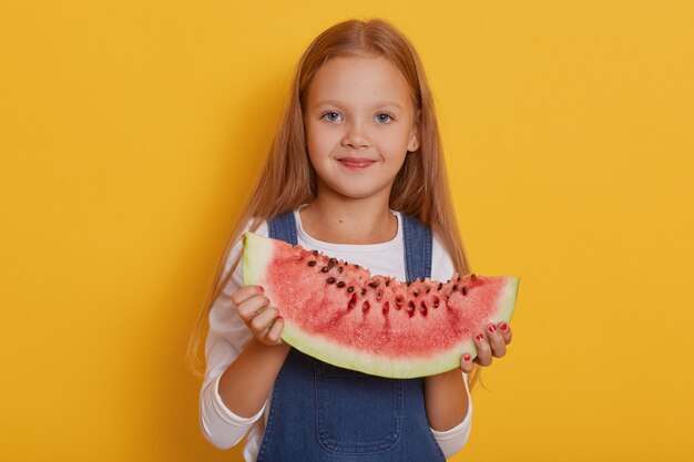Foto interior da menina encantadora com uma porção de melancia nas mãos dela