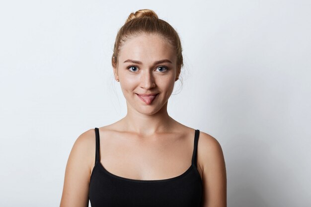 Foto interior de engraçado mulher loira com nó de cabelo, mostrando a língua enquanto discutia com alguém, tentando convencer que ela está certa. Bela modelo feminino mostrando a língua na câmera isolada no branco