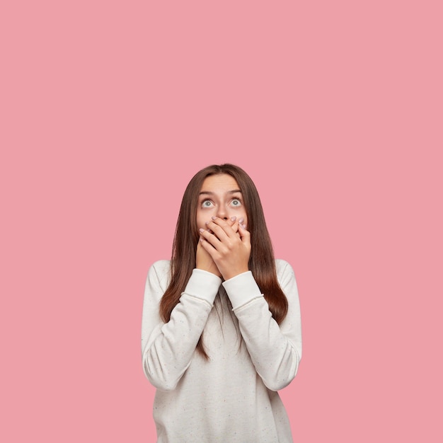 Foto interna da bela morena em choque posando contra a parede rosa