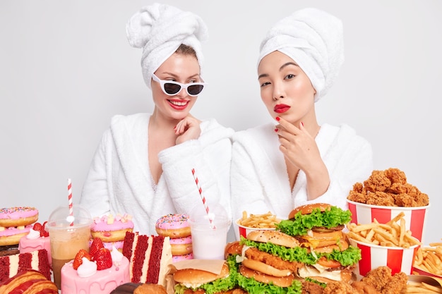 Foto interna de duas mulheres mestiças levando um estilo de vida pouco saudável, comendo junk food e lanches prejudiciais durante a hora das refeições