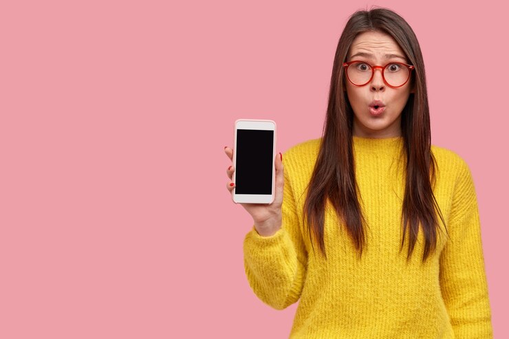 Foto grátis foto interna de hipster morena surpresa com expressão de espanto mostra celular com tela em branco, vê descontos em gadgets na loja, usa roupas amarelas