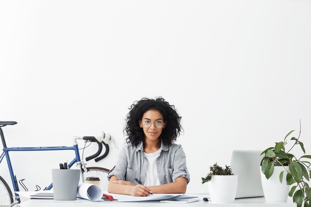 Foto interna de jovens mulheres de pele escura e sorrindo positivamente em uma mesa de escritório