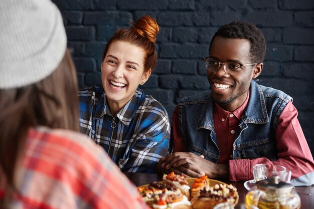 Foto interna de um grupo inter-racial de três jovens elegantes conversando de forma fácil e animada