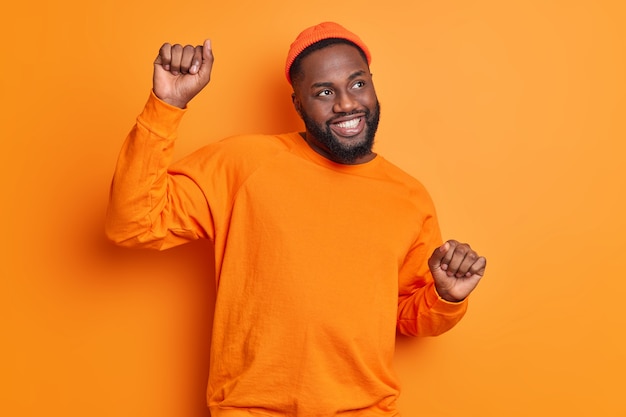 Foto interna de um homem afro-americano de pele escura e positivo apertando as mãos e movendo danças despreocupadas com uma expressão feliz