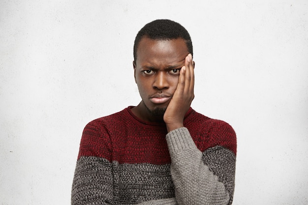 Foto interna de um jovem africano infeliz usando um suéter quente