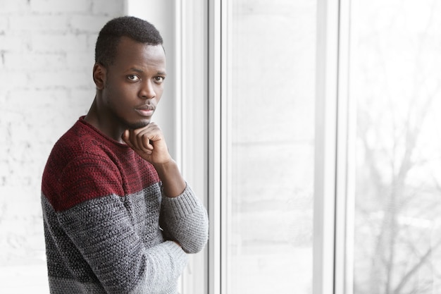 Foto grátis foto interna de um jovem de pele escura vestido casualmente, segurando a mão no queixo