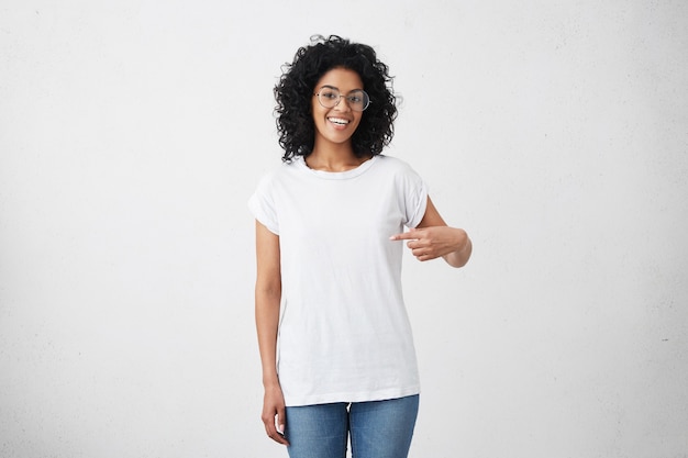 Foto interna de uma jovem afro-americana sorridente e alegre com cabelo encaracolado apontando o dedo indicador