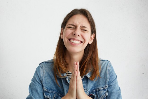 Foto interna de uma jovem ansiosa, mantendo os olhos bem fechados e apertando as mãos