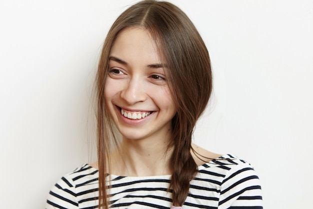 Foto interna de uma jovem morena alegre com uma trança sorrindo alegremente