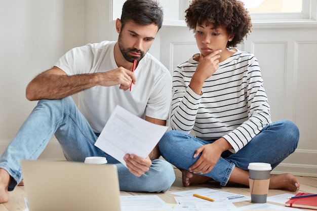 Foto interna de uma mulher e um homem de raça mista séria estudando arranjos particulares, trabalhando em casa