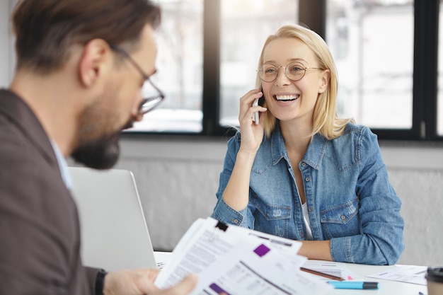 Foto interna de uma mulher loira conversando sobre negócios com um colega