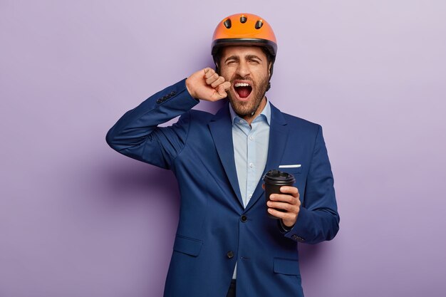 Foto interna do empresário cansado e sobrecarregado de trabalho posando em um terno elegante e capacete vermelho no escritório