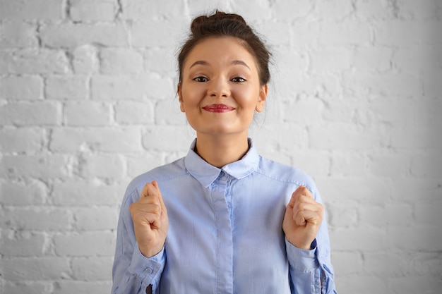 Foto isolada de jovem funcionária feliz muito feliz com o coque de cabelo cerrando os punhos e sorrindo amplamente, animado com a promoção ou aumento de salário. emoções, reações e sentimentos humanos positivos