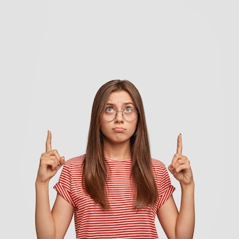 Foto isolada de mulher carrancuda com expressão ofensiva, indica com os dois dedos indicadores