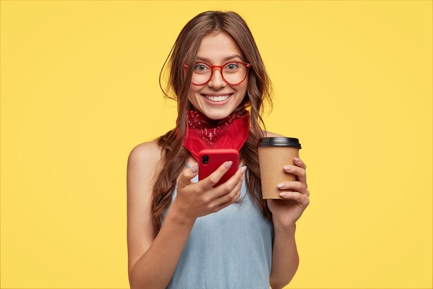 Foto isolada de um jovem bonito e sorridente em alto astral, bebendo café para viagem