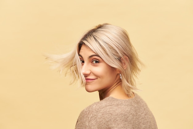 Foto grátis foto isolada de uma jovem atraente e elegante com penteado bob e piercing facial dançando na parede em branco, sorrindo feliz, aproveitando o tempo agradável, se divertindo, com o cabelo loiro voando no vento