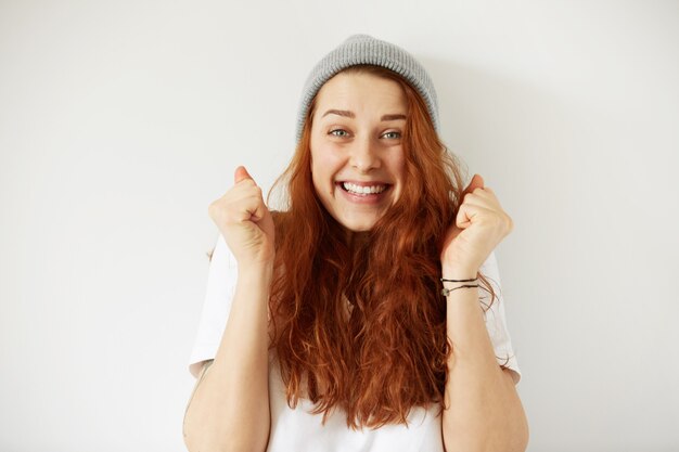 Foto na cabeça de uma jovem mulher feliz usando boné cinza e camiseta com um sorriso alegre e vencedor