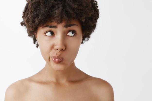 Foto grátis foto na cabeça de uma mulher nua bonita e preocupada, com cabelo encaracolado franzindo os lábios e olhando para o canto superior direito com uma expressão preocupada, hesitando, em dúvida em fazer a escolha certa