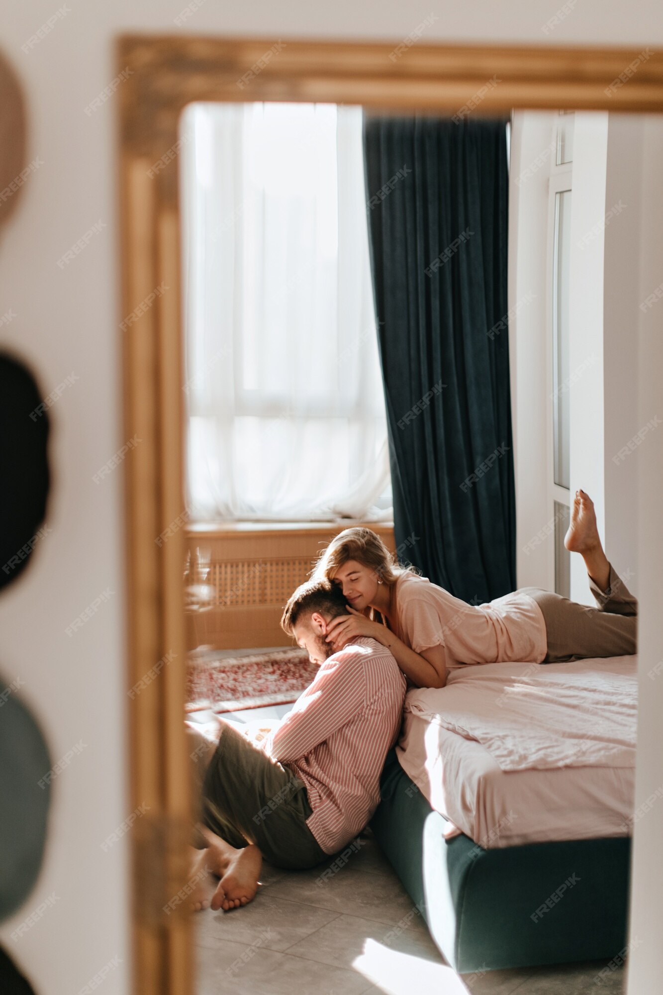 Foto no espelho da menina deitada na cama. senhora com ternura abraçando  seu jovem enquanto ele está sentado no chão.