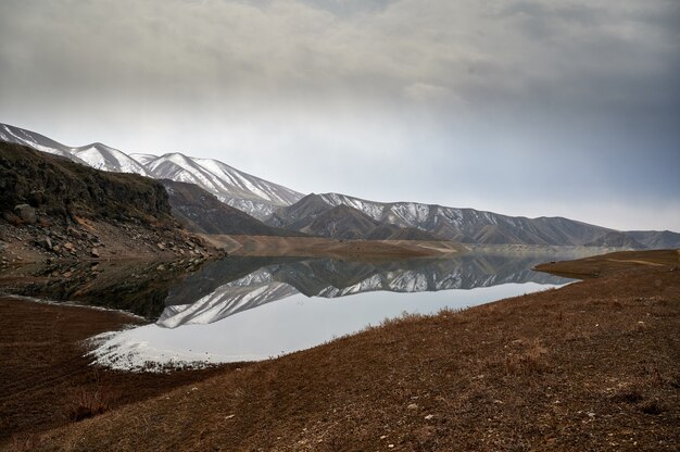 Foto panorâmica horizontal de uma cadeia de montanhas refletida nas águas do reservatório de Azat, na Armênia