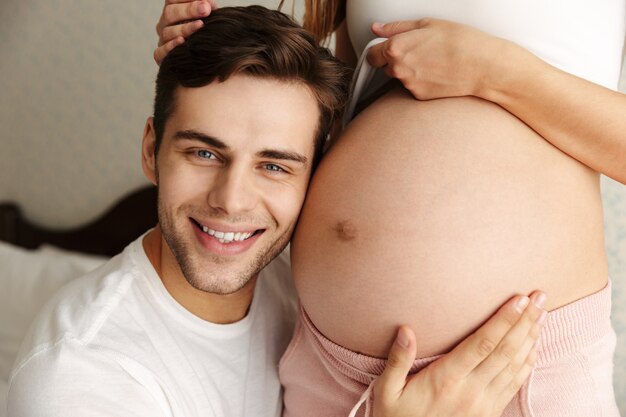 Foto recortada de homem abraço barriga de sua adorável esposa grávida dentro de casa em casa.