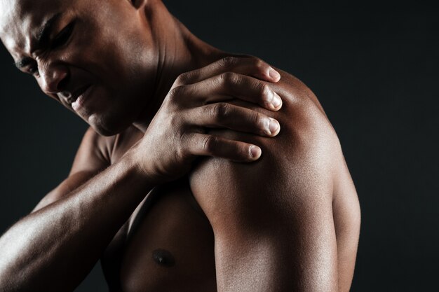 Foto recortada de jovem afro-americano sem camisa com dor no ombro