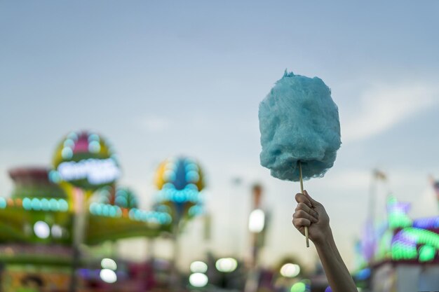 Foto seletiva de uma mulher segurando algodão doce no parque de diversões