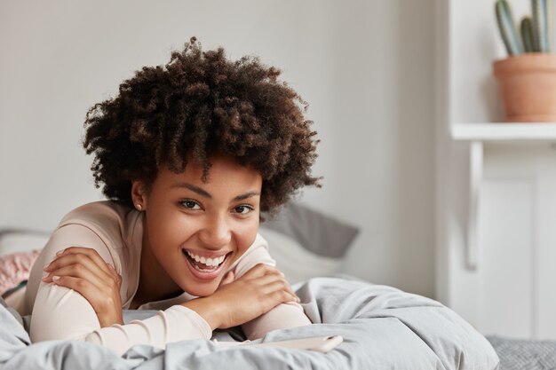 Foto sincera de uma jovem agradável posando em casa em uma cama confortável