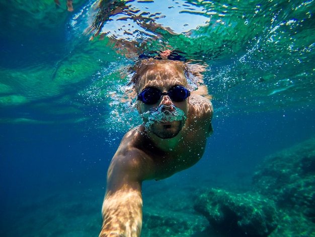 Foto subaquática de um jovem bonito, relaxante e mergulho com snorkel no mar para as férias de verão, enquanto tirava uma selfie.