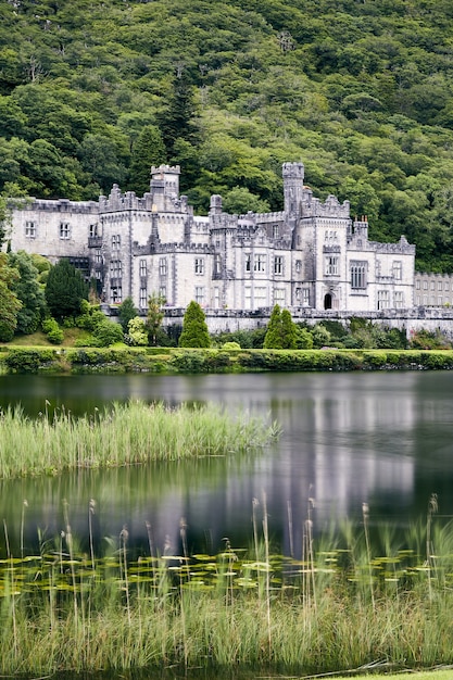 Foto vertical da Abadia de Kylemore na Irlanda, cercada por vegetação e um lago