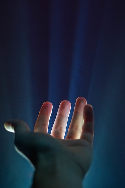 Foto vertical da mão de uma pessoa com uma luz brilhando entre os dedos