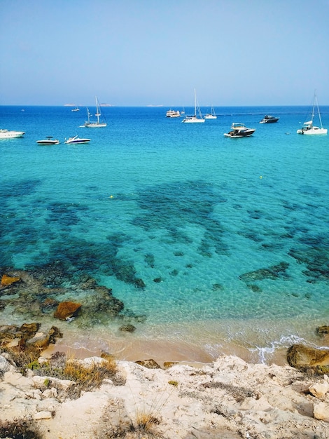 Foto vertical da praia próxima a Ibiza e barcos nela