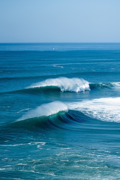 Foto vertical das ondas espumosas do Oceano Atlântico perto do município da Nazaré, em Portugal