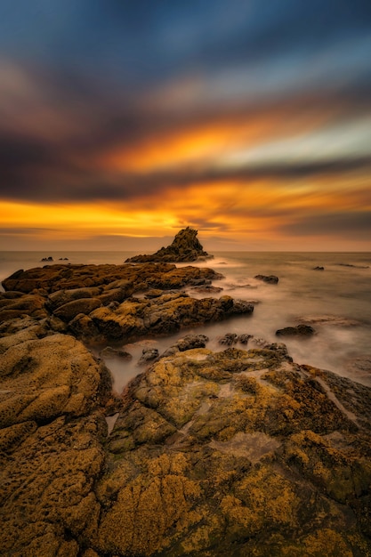 Foto vertical das pedras à beira-mar sob o fantástico nascer do sol