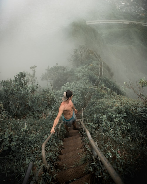 Foto vertical de alto ângulo de um homem parado na escada olhando as montanhas enevoadas