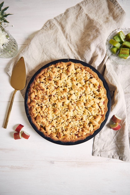 Foto vertical de alto ângulo de um prato de torta de bolo Rhabarbar crocante e alguns ingredientes em uma mesa