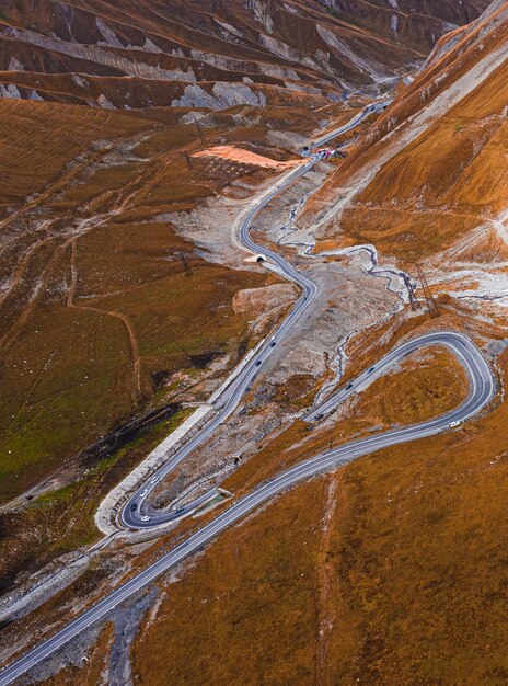 Foto vertical de alto ângulo de uma estrada de asfalto estreita passando por colinas cobertas de grama