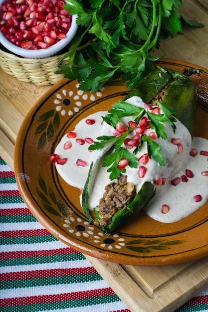 Foto vertical de Chiles en nogada em um prato sobre uma placa de madeira sobre a mesa