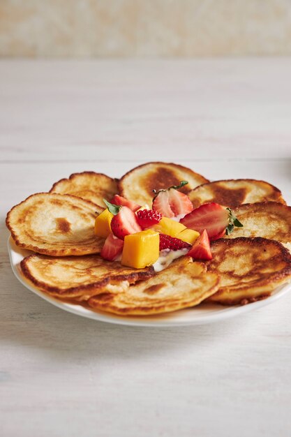 Foto vertical de deliciosas panquecas com frutas na mesa de madeira branca