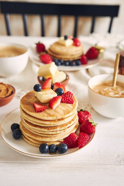 Foto vertical de deliciosas panquecas veganas de tofu com frutas coloridas, xarope e café