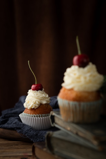 Foto vertical de deliciosos bolinhos com creme e cerejas por cima