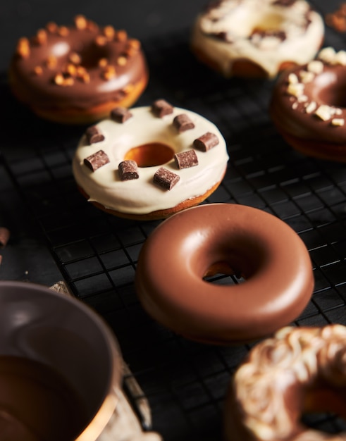 Foto vertical de deliciosos donuts cobertos de esmalte e pedaços de chocolate em uma mesa preta