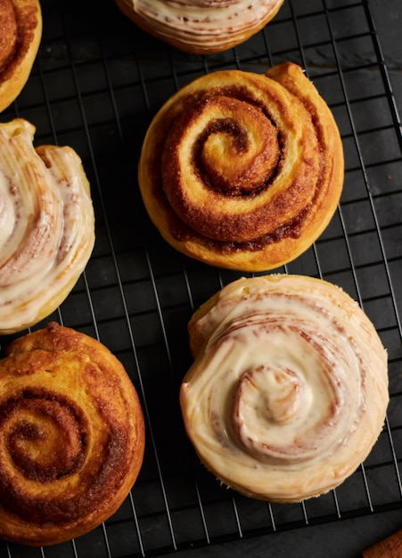 Foto vertical de deliciosos rolinhos de canela cobertos com esmalte branco em uma mesa preta